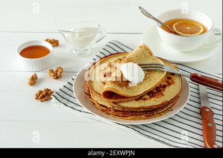 Pfannkuchen mit Honigsirup und saurer Sahne auf einem weißen Teller serviert. Traditionelle Crepes für Pancake Week oder Shrovetide Stockfoto