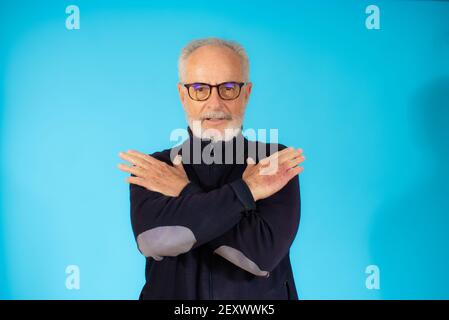 Grauhaarige ältere Mann trägt lässigen Pullover und Brille auf blauem Hintergrund Ablehnung Ausdruck Kreuzung Arme und Handflächen tun negative Zeichen. Stockfoto