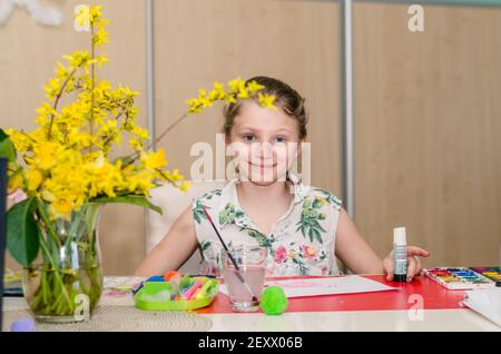 Liebenswert blonde Mädchen auf dem Tisch sitzen und erstellen ostern Handwerk Stockfoto