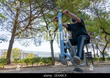 Stock Foto von Mann trägt Gesichtsmaske tun Training im Park mit Sportmaschine. Stockfoto