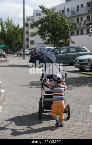 POZNAN, POLEN - 06. Aug 2017: Kleiner Junge schiebt einen Buggy mit Baby auf einen Bürgersteig Stockfoto