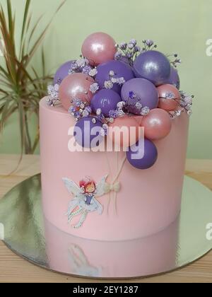 Lila-rosa festliche schöne Kuchen mit Ballons und ein Mädchen auf dem Hintergrund einer Pflanze. Vertikales Foto. Stockfoto