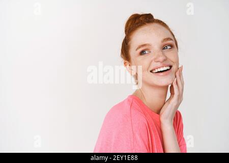 Schönheit und Hautpflege. Lächelndes Mädchen mit Ingwer-Haar gekämmt in chaotischen Brötchen, berühren perfekte und leuchtende Haut und lächelnd, zeigt Gesicht ohne Make-up Stockfoto