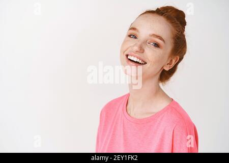 Hautpflege- und Make-up-Konzept. Glückliche junge Frau mit Ingwer-Haar gekämmt in chaotischen Brötchen, natürliche Make-up und Sommersprossen, lachen und zeigt weiße Zähne Stockfoto