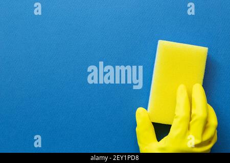 Hand in gelbem Handschuh halten Schwamm auf blauem Hintergrund. Reinigungskonzept. Draufsicht, Kopierraum Stockfoto