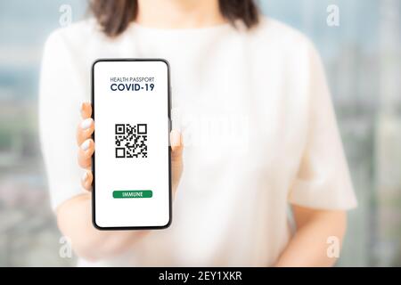 Frau mit Smartphone mit Covid-19 Gesundheitsausweis. Coronavirus-Impfungen zertifiziertes App-Interface-Konzept mit qr-Code auf dem Smartphone bei Frau han Stockfoto