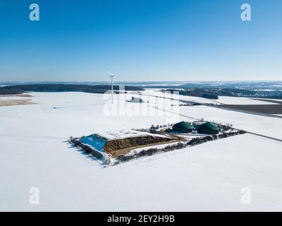 Luftaufnahme auf Biogasanlage und Windkraftanlage in ländlichen Deutschland im Winter Schnee an einem sonnigen Tag mit großen Blauer Himmel Stockfoto