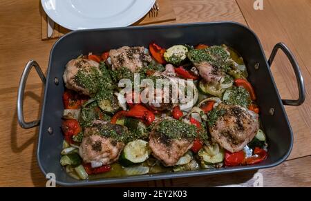 Blech Backen von gebratenen Hähnchenschenkeln mit Kräuter Belag und Gemüse einschließlich Zucchini und Paprika in einem Bräter Stockfoto