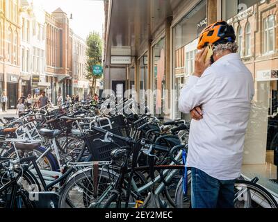 Haarlem, Niederlande - 21. Aug 2018: Rückansicht eines Holländers mit Fahrradhelm auf dem Fahrradparkplatz, der auf dem Smartphone spricht Stockfoto