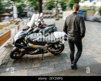 Den Haag, Niederlande - 21. Aug 2018: Unfokussierte Ansicht eines jungen Mannes mit Lederbiker-Kleidung, der in der Nähe der geparkten Motorräder läuft Stockfoto