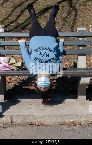 Eine asiatisch-amerikanische Frau, wahrscheinlich Chinesin, macht eine sehr ungewöhnliche Strecke auf dem Kopf auf einer Bank in einem Park in Queens, New York City Stockfoto