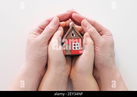 Immobilien und Familienhaus Konzept - Nahaufnahme Bild von Kind und Frau Hände halten roten Papierhaus mit Familie. Hochwertige Fotos