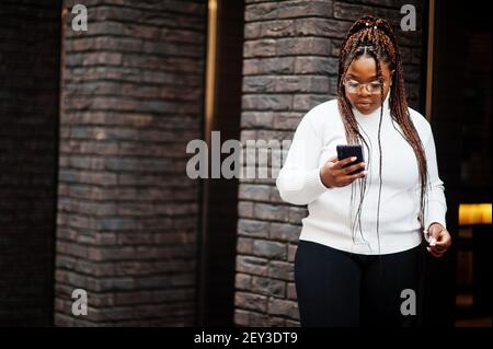 Glamouröse afroamerikanische Frau in weißen Rollkragenpullover Pose auf der Straße mit Handy. Stockfoto