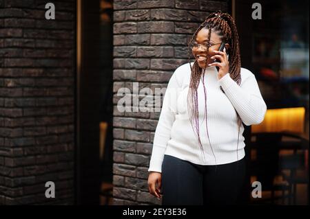 Glamouröse afroamerikanische Frau in weißen Rollkragenpullover Pose auf der Straße mit Handy. Stockfoto