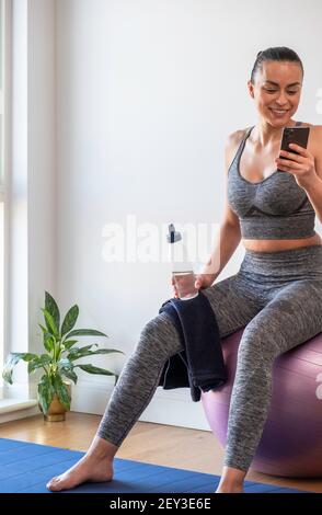 Attraktive Frau, die sich nach Yoga ausruhte und ihr Telefon überprüfte Stockfoto