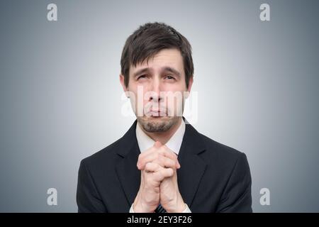 Lustiger junger Geschäftsmann bettelt oder bittet um Hilfe. Stockfoto