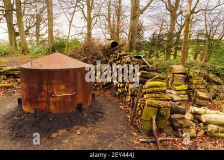 Ein traditioneller Holzkohlebrenner Ofen oder Ofen und ein Stapel Von Baumstämmen in einer Waldlichtung in Nordwales für Herstellung von traditionellen Holzkohle Brennstoff Stockfoto