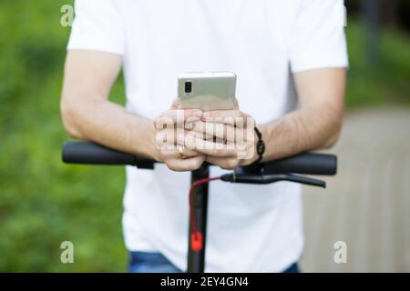 Junger Mann im Hut verwenden Handy, online-Verleih Elektroroller in der Stadt zu buchen. Innovativer Verkehr Stockfoto
