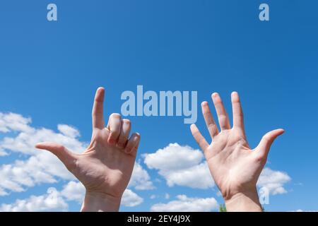 Geste Nahaufnahme der Hand einer Frau zeigt eine offene Handfläche und zwei Finger oben isoliert auf einem blauen Himmel Hintergrund mit Wolken, Nummer sieben ist Zeichen languag Stockfoto