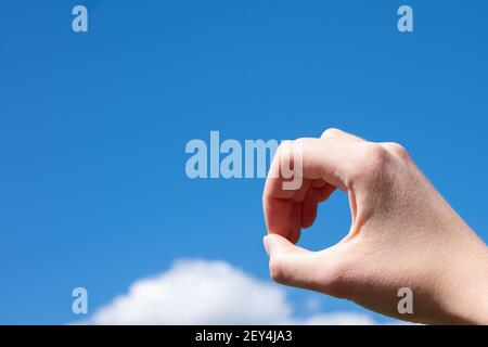Nahaufnahme Geste einer Frau Hand machen einen Ring von Fingern isoliert auf einem Hintergrund des blauen Himmels mit Wolken. Stockfoto