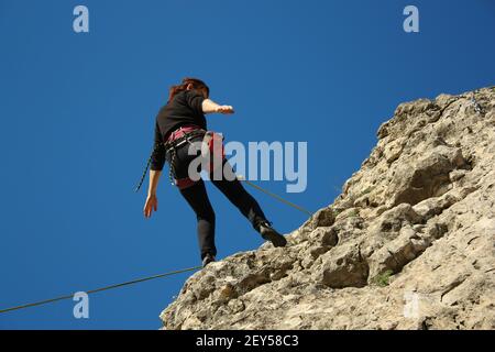 Eine Frau steigt von einer Klippe herab, steht mit dem Rücken, Foto von unten Stockfoto