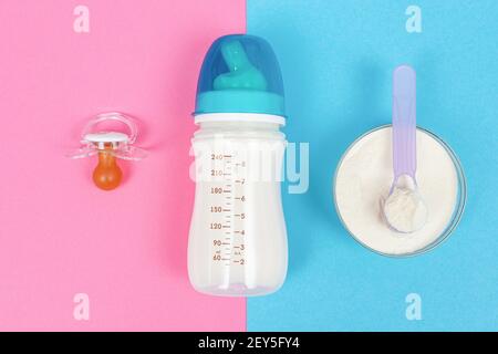 Flasche Milch für Neugeborene, Schnuller auf rosa Hintergrund und Glas mit Milchpulver auf blauem Hintergrund. Babyfütterung Konzept. Zwei Seiten Stockfoto