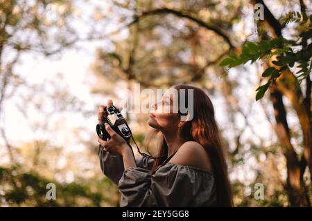 Junge Frau fotografiert mit Kamera, während sie im Sommerwald steht Stockfoto