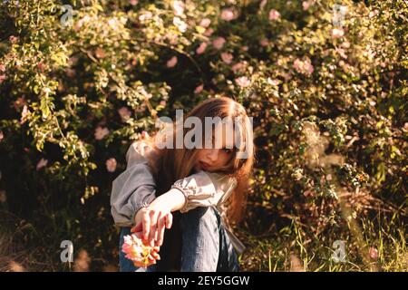 Teenager-Mädchen sitzt inmitten von Blumen im Park im Sommer Stockfoto