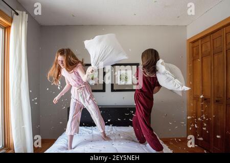 Zwei glückliche junge Mädchen, die einen Federkissen Kampf auf dem Bett haben. Stockfoto