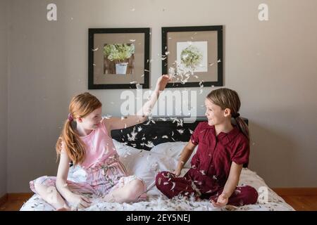 Zwei glückliche junge Mädchen, die einen Federkissen Kampf auf dem Bett haben.