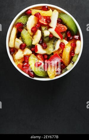Frischer Obstsalatbecher aus saftigen Früchten auf schwarzem Hintergrund. Freier Speicherplatz für Text. Scheiben von frischen, saftigen und gesunden Früchten für eine gesunde Ernährung. Stockfoto