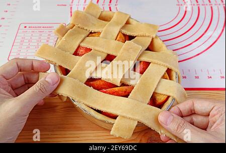 Hand des Mannes weben Stücke des geschnittenen Teigs auf Kuchenplatte Für das Gitter der oberen Kruste des Apfelkuchens Stockfoto