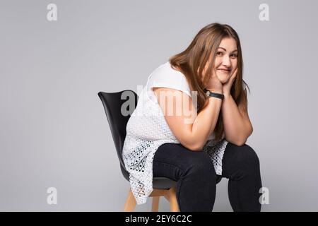 Menschen, Lebensstil, Übergewicht und Körper Positivität Konzept. Nette attraktive, freundliche junge Frau, die auf einem Stuhl sitzt und beim Arbeiten fröhlich lächelt Stockfoto