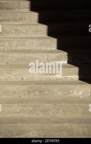 Schatten, die durch das Sonnenlicht am Nachmittag in der Tagessonne auf die Außentreppe aus Zement geworfen werden, wodurch eine optische Illusion von Dunkelheit, Leerheitswinkeln oder Wellung entsteht Stockfoto