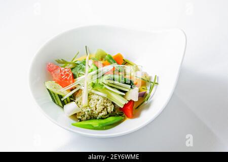 Ein weißer Teller auf weißer Tischdecke mit Lauch-Couscous-Salat, Gurken, Tomaten, Brokkoli, Schneeerbsen und Paprika Stockfoto