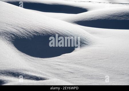 Horizontales Bild von Schneehügeln im Winter mit Schatten, die durch Sonnenlicht geworfen werden und wie Löcher in schneeweichen kleinen Schneehügeln aussehen, horizontaler Hintergrund Stockfoto