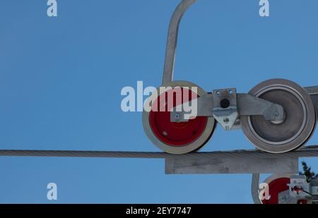 Nahaufnahme von runden Rädern von Sessellift-Riemenscheiben auf industriellem großem Kabel zwei Räder ein roter, ein grauer oder silberblauer Himmel in horizontalem Hintergrund Stockfoto