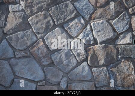 Zufällig seltsam geformte natürliche Steine oder Felsen in der Außensteinmauer oder Felswand Stützmauer oder Haus Außenmauerwerk Hintergrund durch Mauerwerk horizontal Stockfoto