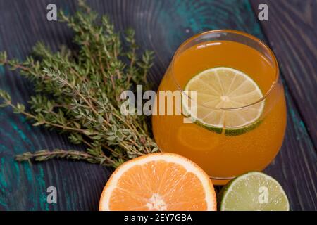 Ein Glas Alkohol. Dekoriert mit einem Limettenkeil. In der Nähe Hälften von Limette, Orange und Thymian. Stockfoto