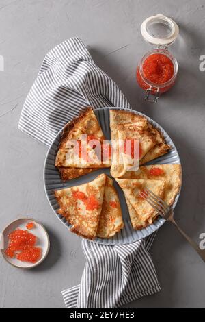 Russische dünne Pfannkuchen oder Blini mit rotem Kaviar auf grauem Teller. Draufsicht. Vertikales Format. Fasching. Stockfoto