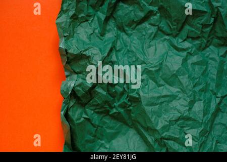 Leerer Papierhintergrund. Grün zerknittertes Papier auf einem orangen Hintergrund.Olive grün leeres Papier Hintergrund, Tapete, Ort für Text.Kreatives leeres Papier Stockfoto