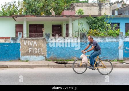 Kubanischer Mann, der mit dem Fahrrad an einem Viva Fidel Schild fährt, Santa Clara, Kuba Stockfoto