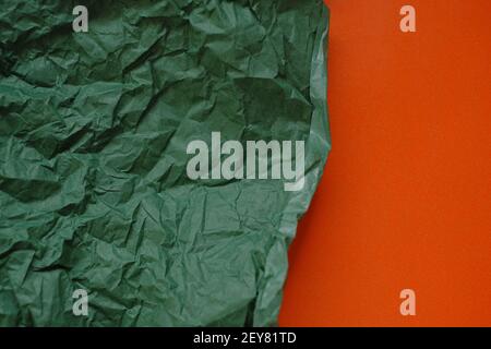 Leerer Papierhintergrund. Grün zerknittertes Papier auf einem orangen Hintergrund.Olive grün leeres Papier Hintergrund, Tapete, Ort für Text.Kreatives leeres Papier Stockfoto