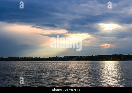 Der Sonnenstrahl schaut durch dunkle Wolken und beleuchtet das Wasser des Seenwaldes in der Ferne. Stockfoto