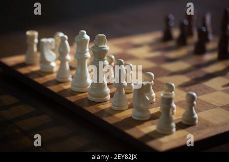 Schachfiguren auf einem Schachbrett werfen lange Schatten. Stockfoto