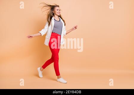 In voller Länge Profil Foto von schönen Dame gehen Wind Schlag Haar tragen Anzug weiß Blazer isoliert pastellbeige Farbe Hintergrund Stockfoto