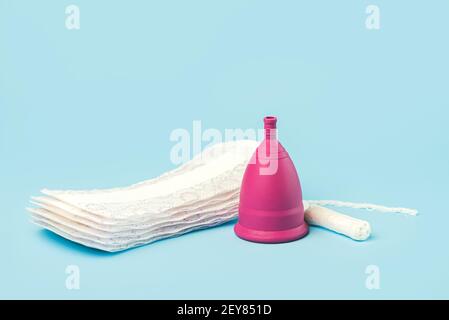 Silikon Menstruationstasse mit Tampon und Menstruationsbeschwerden oder Servietten auf blauem Hintergrund.weibliche intime Alternative gynäkologische Hygiene conce Stockfoto