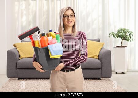 Junge Frau in einem Wohnzimmer hält einen Eimer mit Reinigungszubehör Stockfoto