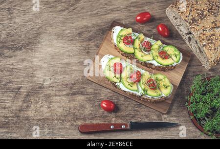 Sandwiches mit Weichkäse, Avocado-Scheiben, Kirschtomaten und Brunnenkresse Sprossen, Getreidebrot und Microgreens in einer Schüssel auf einem alten Holztisch, zu Stockfoto