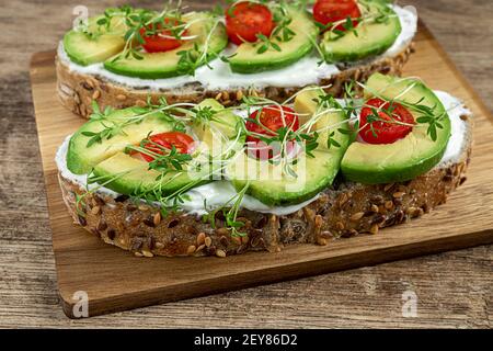 Gesunde Snacks mit Microgreens - Cerealien Brot Sandwiches mit Weichkäse, Avocado Scheiben, cherri Tomaten und Brunnenkresse Sprossen Stockfoto